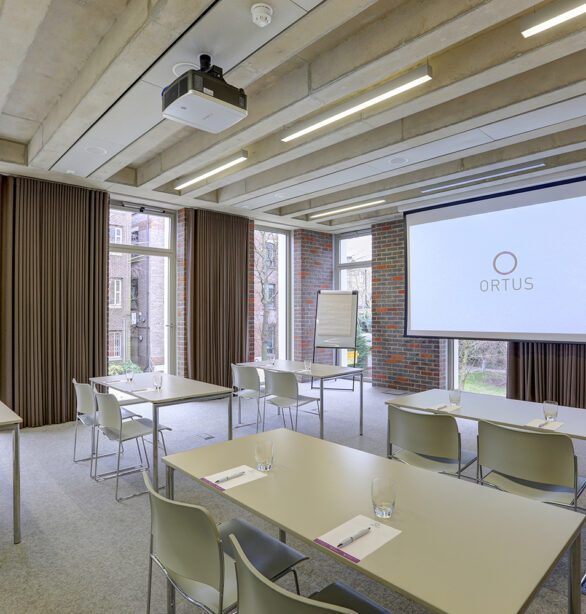 Interior of a meeting room with a screen and rows of tables and chairs